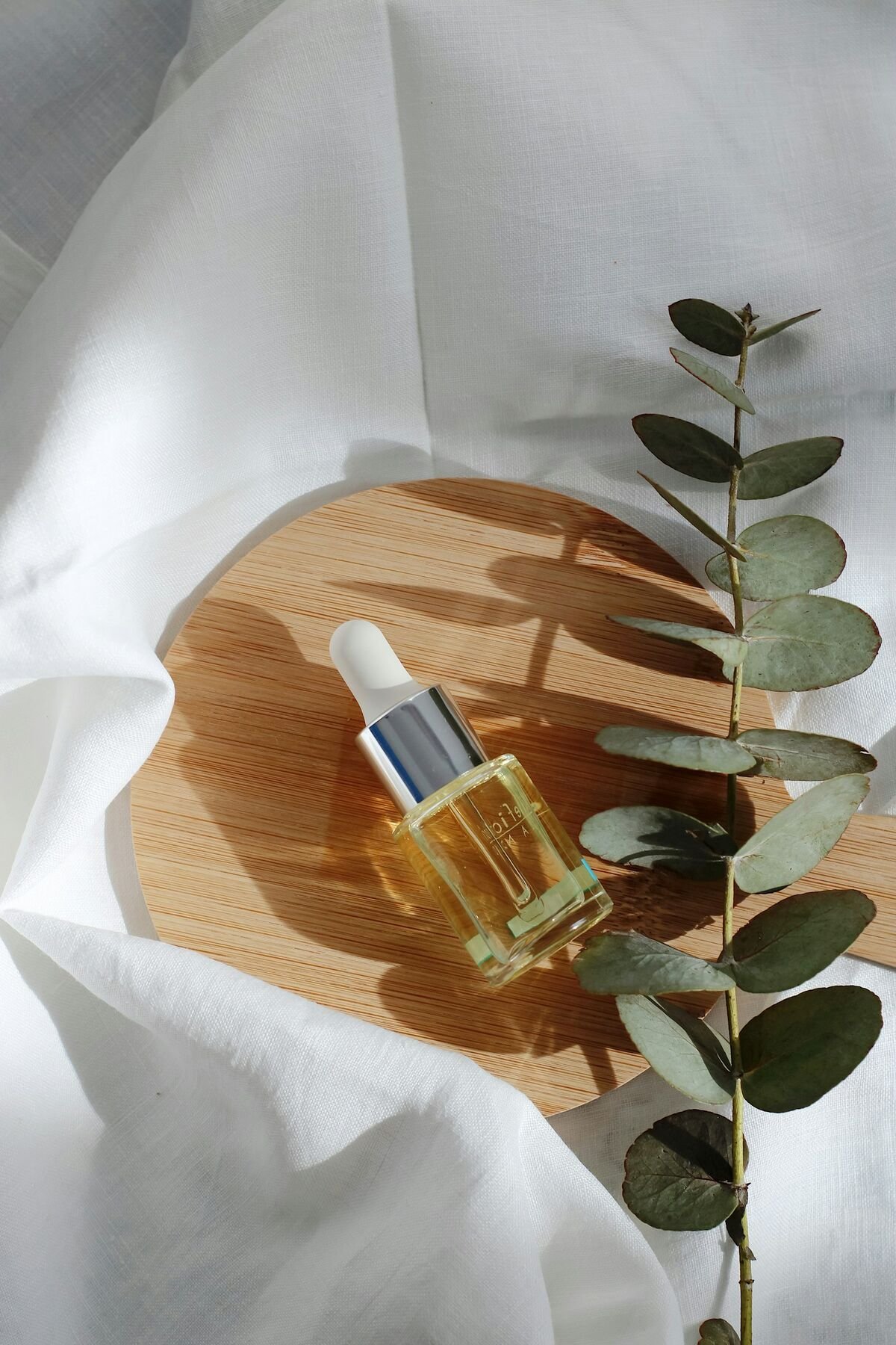 A skincare oil dropper bottle on linen with eucalyptus leaves